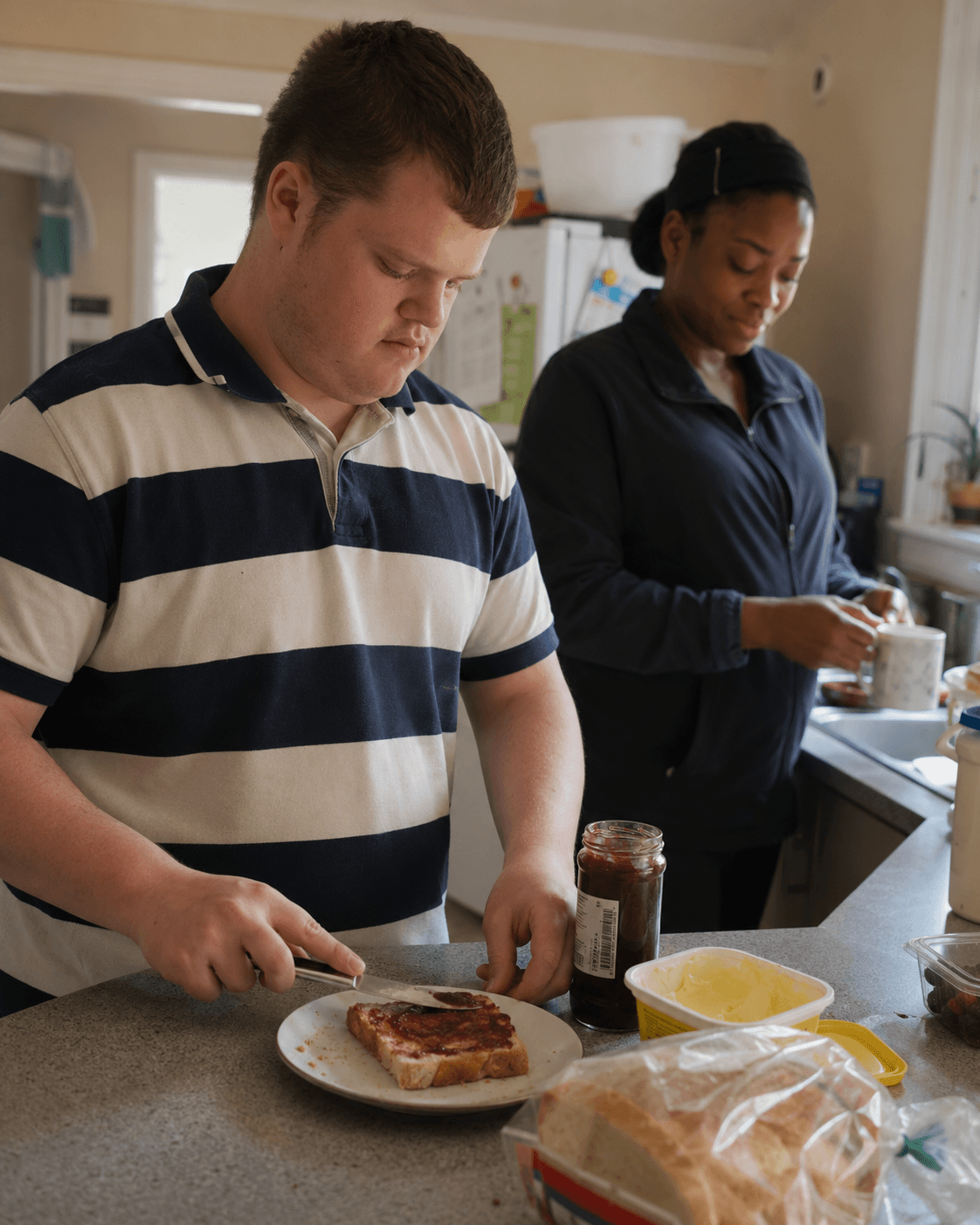 A young adult and support worker preparing breakfast in a home kitchen